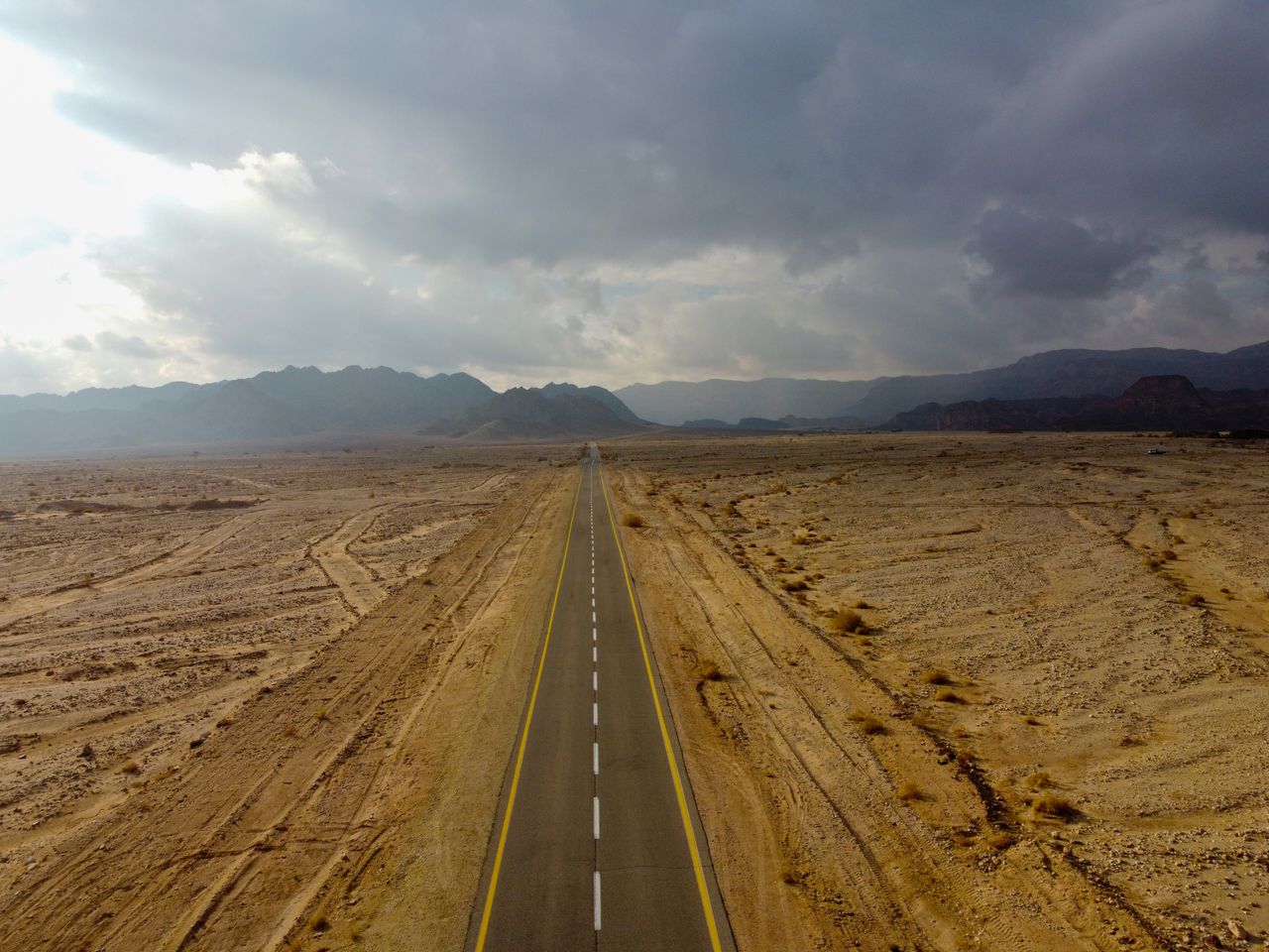 An aerial view of a long, empty road stretching through the arid Nevada desert under cloudy skies.