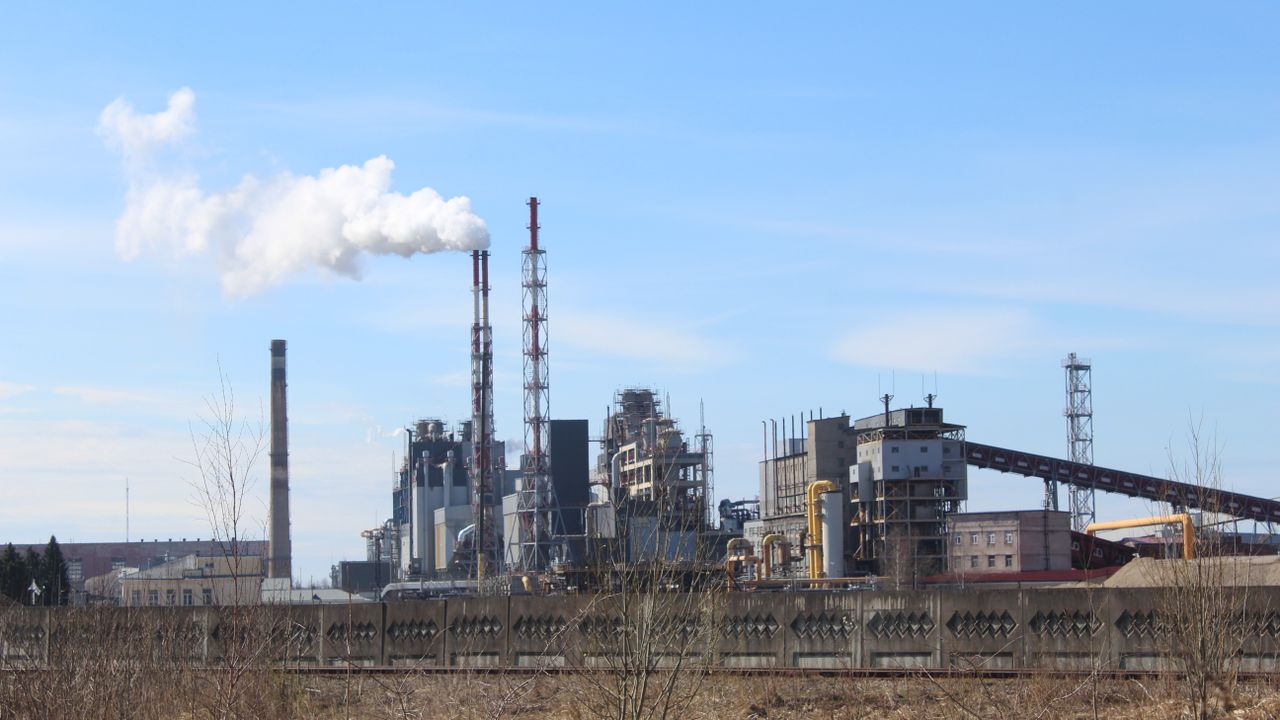An industrial factory with smoke emissions against a clear blue sky.