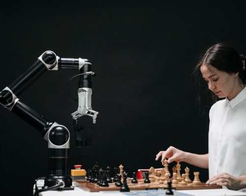 pexels-photo-8438951-8438951 A woman plays chess against a robotic arm, showcasing AI innovation in a modern setting.